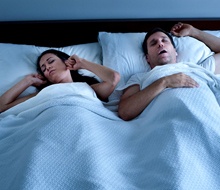 A woman covering her ears and her partner snoring
