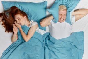 young man frustrated with woman snoring loudly from sleep apnea